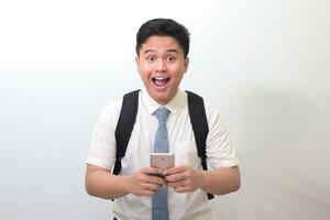 Indonesian senior high school student wearing white shirt uniform with gray tie showing shocked face expression while holding a mobile phone. Isolated image on white background photo