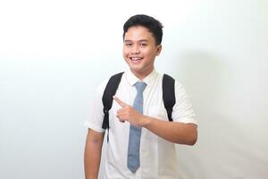 Indonesian senior high school student wearing white shirt uniform with gray tie showing product, pointing at something and smiling. Isolated image on white background photo