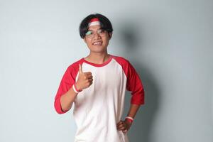 retrato de atractivo asiático hombre en camiseta con rojo y blanco cinta en cabeza, demostración bueno trabajo mano gesto con pulgares arriba. aislado imagen en gris antecedentes foto
