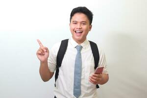 Indonesian senior high school student wearing white shirt uniform with gray tie showing and presenting mobile phone while pointing away with finger. Isolated image on white background photo