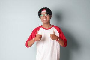 retrato de atractivo asiático hombre en camiseta con rojo y blanco cinta en cabeza, demostración bueno trabajo mano gesto con pulgares arriba. aislado imagen en gris antecedentes foto