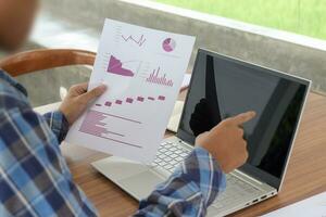 Close up of male freelance worker hand working on laptop and pointing with finger on analysis data with business graph and chart of information diagram on office desk in the morning photo