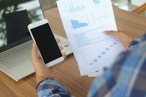 Close up of male freelance worker hand working on laptop and pointing with finger on analysis data with business graph and chart of information diagram on office desk in the morning photo