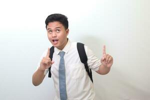 Indonesian senior high school student wearing white shirt uniform with gray tie showing product, pointing at something and smiling. Isolated image on white background photo