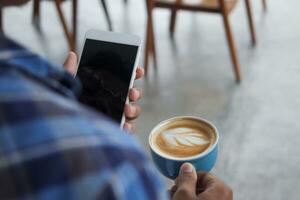 Close up of Asian man holding a cup of coffee and mobile phone. Technology and morning routine concept photo