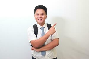 Indonesian senior high school student wearing white shirt uniform with gray tie showing product, pointing at something and smiling. Isolated image on white background photo