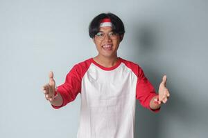 Portrait of attractive Asian man in t-shirt with red and white ribbon on head, reaching out for a handshake and greet someone. Isolated image on gray background photo