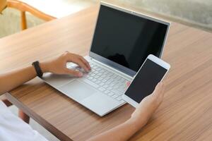 Close up of businessman hand touching blank screen of mobile phone with laptop beside on the table.  Display of smartphone and laptop mock up photo