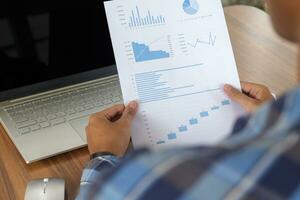 Close up of male freelance worker hand working on laptop and pointing with finger on analysis data with business graph and chart of information diagram on office desk in the morning photo