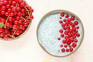 Fresh red currant berries and overnight chia seed pudding in a coconut bowl. Close up, top view, flat lay. Healthy raw food concept. Pink background, copy space. photo