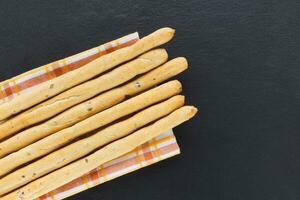 Fresh Italian Grissini Breadsticks served on black background. Dry baked bread with olive pieces on slate plate. Top view, copy space photo