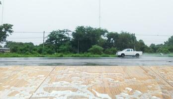 de madera mesa con lluvia que cae en eso borroso antecedentes de un coche conducción en el la carretera en el lluvia. vacío espacio para mostrando productos foto