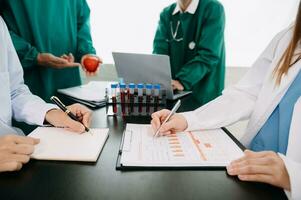Medical team having a meeting with doctors in white lab coats and surgical scrubs seated at a table discussing a patients working online using computers in the medical industry photo