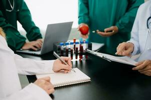 Medical team having a meeting with doctors in white lab coats and surgical scrubs seated at a table discussing a patients working online using computers in the medical industry photo
