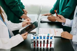 Medical team having a meeting with doctors in white lab coats and surgical scrubs seated at a table discussing a patients working online using computers in the medical industry photo