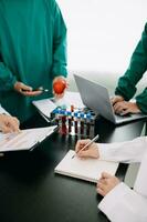 Medical team having a meeting with doctors in white lab coats and surgical scrubs seated at a table discussing a patients working online using computers in the medical industry photo