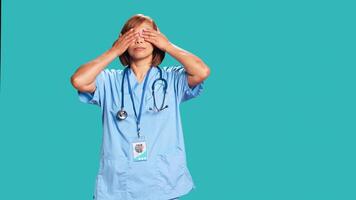 Healthcare expert covering eyes, ears and mouth with hands, imitating the three wise monkeys. Licensed nurse showing don t see, don t hear and don t speak concept, isolated over studio background photo