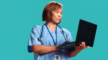 Close up shot of experienced healthcare expert imputing patient data on laptop after finishing clinical checkup appointment. Nurse typing informations on notebook, isolated over studio background photo
