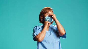 Close up shot of asian clinic employee putting on medical face mask before starting hospital job shift. BIPOC nurse isolated over studio background avoiding virus spreading by wearing protective gear photo