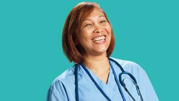Upbeat chilled asian clinic worker having burst of laughter while at work. Close up of happy nurse enjoying amusing discussion with colleague during shift break, isolated over studio background photo
