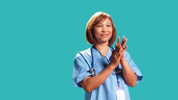 Approving smiling nurse happily clapping hands, pleased with achievements. Clinic employee cheering, doing applauding gesture while at work, isolated over studio background, close up photo