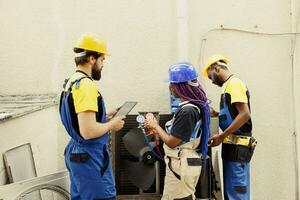 Competent mechanics diverse team hired by client to search for refrigerant leaks on outdoor air conditioner evaporator coil leading to poor cooling issues during hot summer months photo