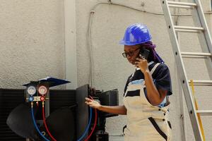 African american apprentice calling manager to inquire about necessary condenser components needing to be replaced. Electrician checking maintenance plan after fixing bad wiring issues photo