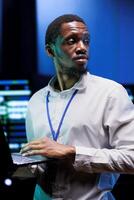 African american expert troubleshooting server farm providing vast computing resources and storage. High tech facility enabling artificial intelligence to process massive datasets for training photo