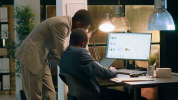 Coworkers in office crosschecking datasets, comparing financial charts and checking business figures during nightshift. Experienced businessmen helping eachother finish project tasks faster photo