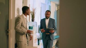 African american business manager checking up on employee project task progress during nightshift break. Relaxed office clerk enjoying cup of coffee, chatting with supervisor by the water tank photo