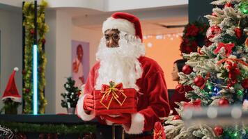 Elderly couple in xmas decorated clothing store giving raffle ticket to worker dressed as Santa Claus holding gift acting as collecting box. Employee organising Christmas promotion event photo