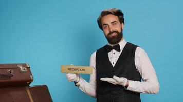 Hotel staff uses reception indicator on camera, guiding people in the right direction. Classy doorkeeper working in hospitality industry, presenting front desk pointer in studio to guide guests. photo