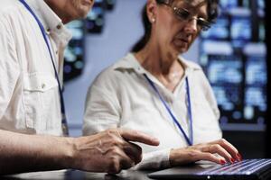 Elderly technical support consultants working to maintain uptime in high tech place. Skilled specialists brainstorming solutions to data center server racks crashing, trying to fix components photo