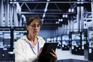 Senescent developer updating data center equipment, writing intricate binary code scripts on tablet, using programming to fortify cybersecurity in technically advanced server hub photo