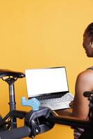 Closeup shot of laptop with isolated chromakey template carried by african american female. In front of yellow background, black person is holding wireless computer displaying blank whitescreen. photo