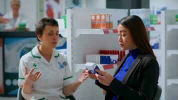 Experienced pharmacist in drugstore with patient prescribing her medical products to treat disease symptoms. Asian woman receiving medical indications from healthcare practitioner photo