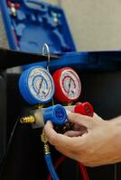 Close up of expert repairman calibrating manifold measurement device during comissioned external air conditioner maintenance. Professional worker looking for low freon levels in cooling system photo