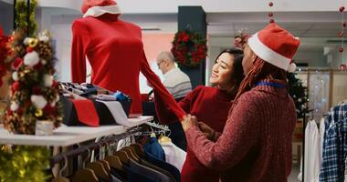 Friendly retail assistant in festive ornate shopping mall fashion shop showing client beautiful red garments, ready to be worn at Xmas themed holiday events during winter season photo
