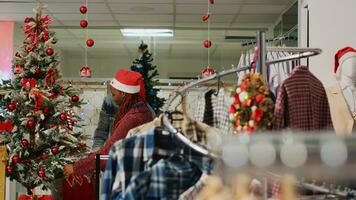 African american employees wearing Santa hat ornating Christmas tree in clothing store before festive promotional event. Retail assitants ornating fashion shop during winter holiday season photo