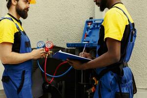 Seasoned specialists employed to do air conditioner check, refilling freon. African american engineer and coworker using manifold gauges to perfectly measure the pressure in condenser photo