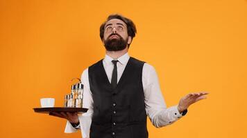 Optimistic butler praying to lord on camera, asking for fortune and acting religious in studio. Faithful elegant waiter working at five star restaurant holding tray, feeling positive over background. photo