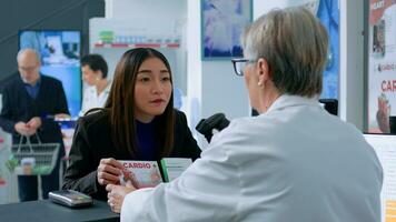 Asian woman in front of drugstore counter checkout asking qualified pharmacist cashier for medical recommendation, trying to pick best pharmaceutical product to counteract illness photo