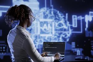 African american engineer updating AI systems, writing intricate binary code scripts on laptop. Tech support using programming to upgrade artificial intelligence simulation model photo