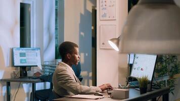 African american manager asking employee to show him company project tasks progress in modern office during nightshift. Management executive crosschecking documents at work photo