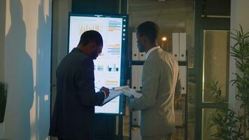 Manager annoyed by lack of project progress in office during nightshift, checking financial charts with employee. Management executive frustrated by slow worker struggling with audit task photo