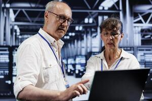 Old engineers preventing strain on data center gadgets caused by AI applications driving up power usage. Knowledgeable technicians maintenancing server racks doing intense computations photo