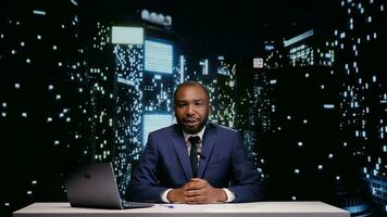 Happy tv host starting night talk show in newsroom, presenting world news and daily events live. African american man broadcasting news segment on midnight television program, reportage. photo