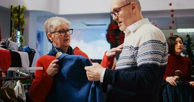 Senior couple browsing through clothes racks in festive adorn clothing store during Christmas shopping spree. Old clients planning to purchase formal attire, enjoying holidays promotional sales photo