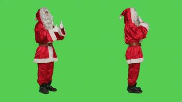 Saint nick in costume does thumbs up standing over full body greenscreen background, expressing like and agreement symbol in studio. Young man in santa suit shows approval sign. photo