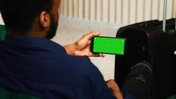 Diverse couple looking at greenscreen display on smartphone, arriving at tropical summer resort and using isolated mockup template. Tourists checking blank chromakey screen in lobby. photo